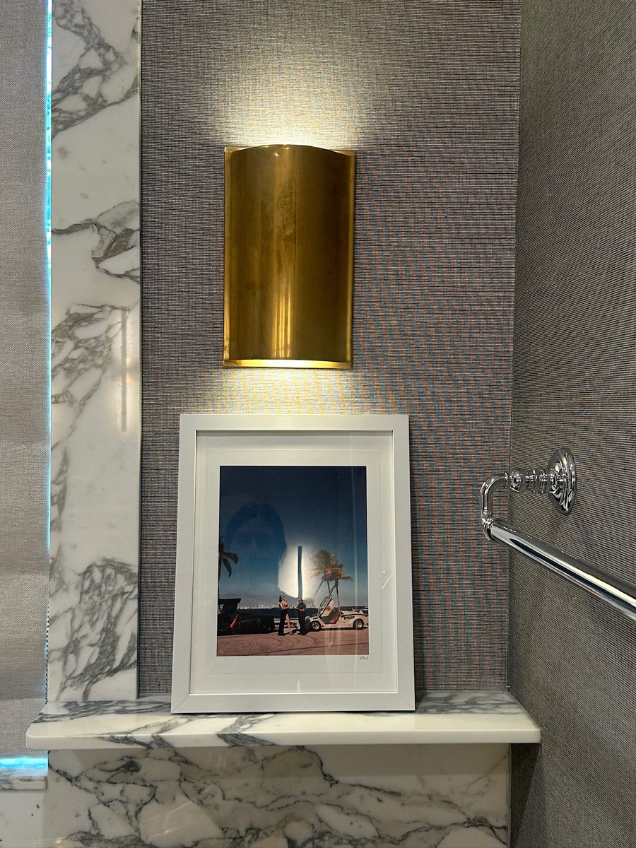 Powder room with gold sconce and framed art on marble ledge